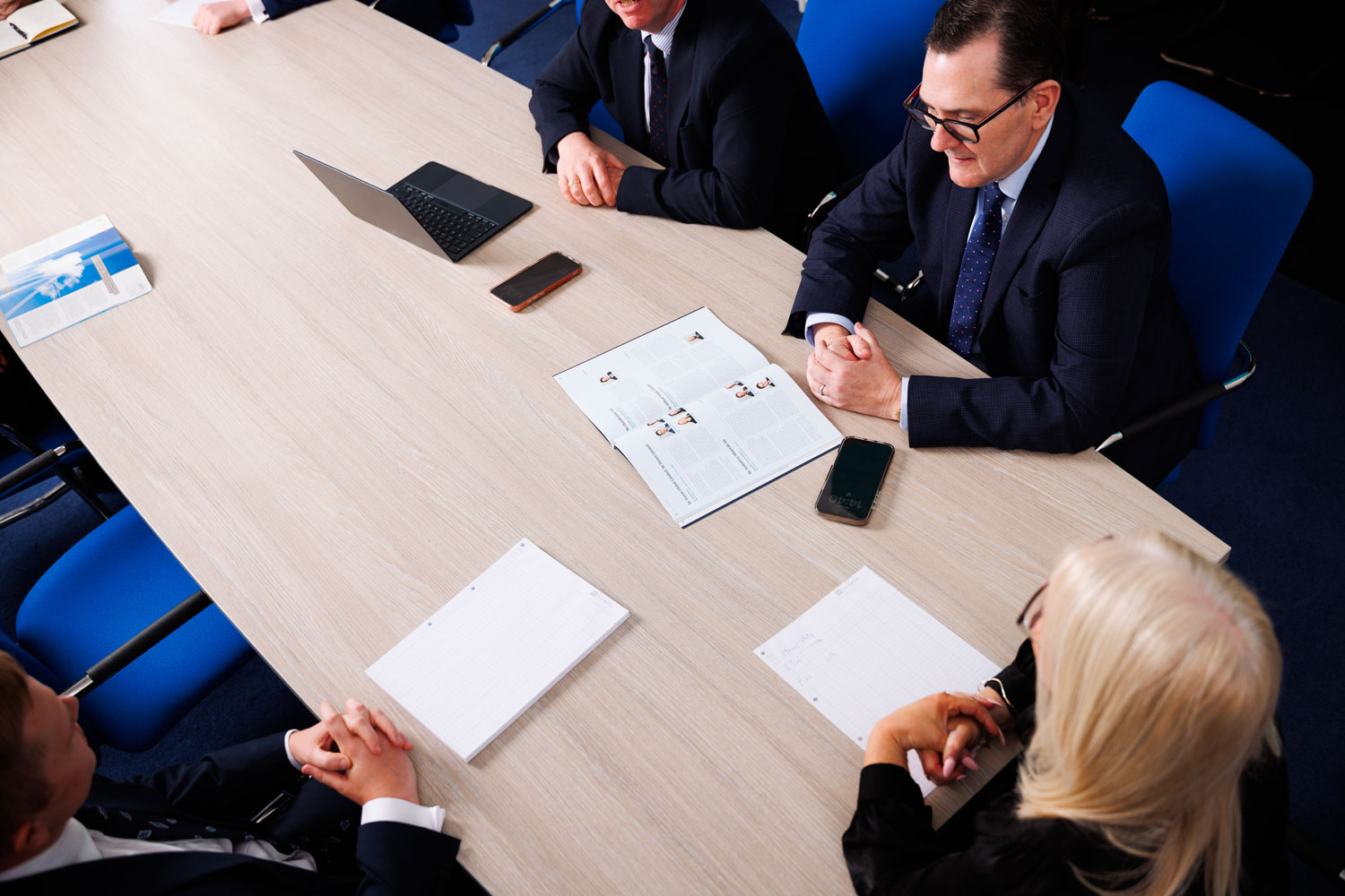Friel Stafford advisors in a boardroom meeting, seated around a table with notepads, a laptop and printed reports.